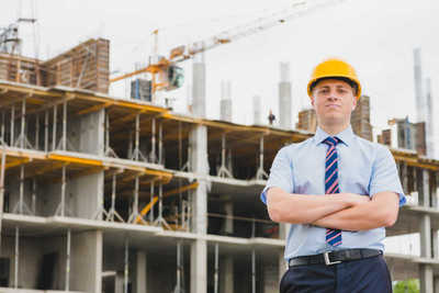 工程师站在建筑前边图片-戴着黄色安全帽的工程师站在未完成建筑前边素材 .